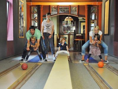 Drei Paare spielen Kegeln in einem gemütlichen Innenraum mit Bögen und Spiegeln.