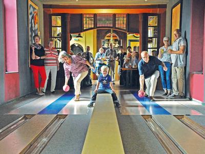 Eine Gruppe von Menschen in einer Kegelbahn, wobei einer gerade eine Kugel wirft.