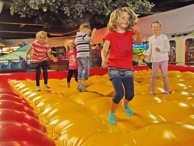 Kinder springen fröhlich auf einer großen, bunten Hüpfburg in einer Halle.