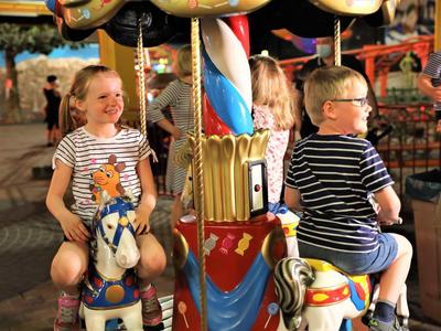 Kinder lachen auf bunten Karussellpferden unter warmem Licht in einem Freizeitpark.