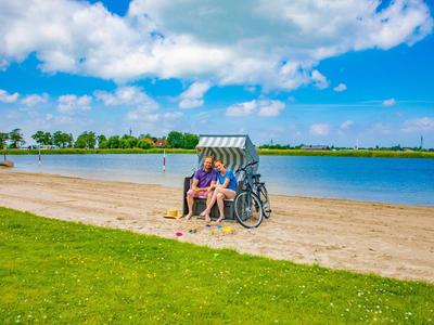Ein Paar sitzt auf einem Strandkorb am Sandstrand mit Blick auf einen See und einen blauen Himmel.