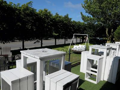 Weiß lackierte Holzmöbel auf grünem Kunstrasen, umgeben von Bäumen und einem Zaun im Garten.