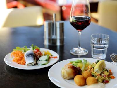 Teller mit Fisch, Gemüse und Kartoffeln, Glas Rotwein und Wasser auf dunklem Tisch.