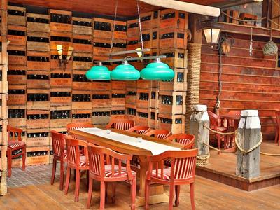 Rustikaler Raum mit Holzwänden, Weinkistenregal, großem Holztisch, roten Stühlen und grünen Hängelampen.