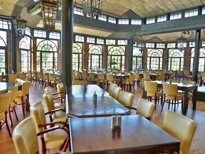 Großer heller Saal mit vielen Tischen und gelben Stühlen, große Fenster und Glasdecke.