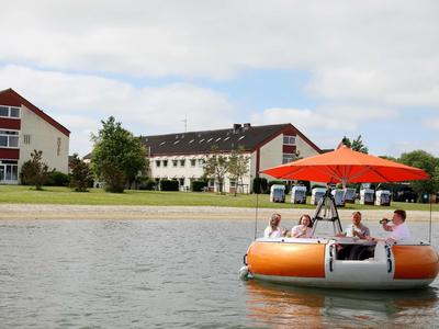 Menschen in einem orangefarbenen Tretboot auf einem See vor Hotelgebäuden
