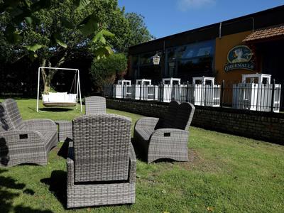 Garten mit grauen Geflechtstühlen und einer weißen Schaukelbank auf grünem Gras vor einem Gebäude.