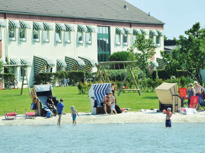 Strand mit Sand, Strandkörben, spielenden Kindern und einem Gebäude im Hintergrund.