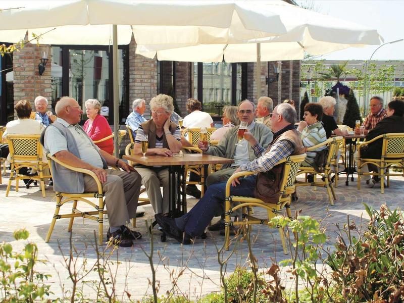 Ältere Menschen sitzen an Tischen unter Sonnenschirmen in einem sonnigen Außenbereich eines Cafés.