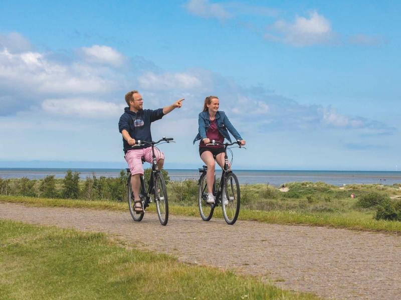 Zwei Männer fahren bei sonnigem Wetter mit Fahrrädern auf einem Weg am Meer entlang.