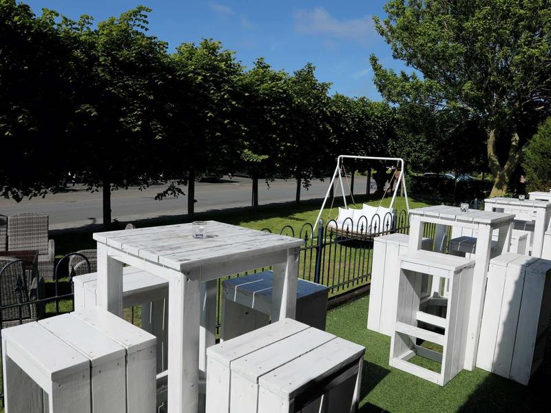 Weiß lackierte Holzmöbel auf grünem Kunstrasen, umgeben von Bäumen und einem Zaun im Garten.