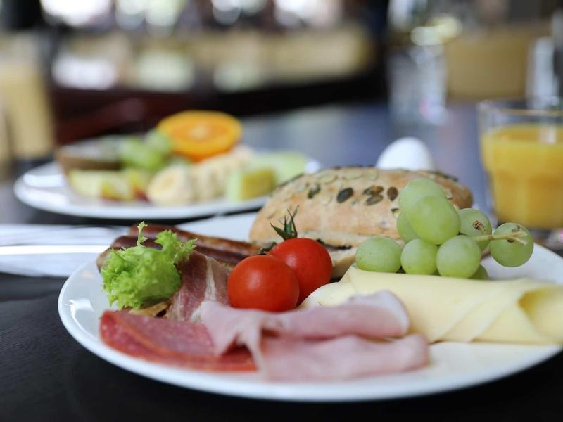 Ein Teller mit Wurst, Käse, Trauben, Tomaten und Brötchen, dazu ein Glas Orangensaft.