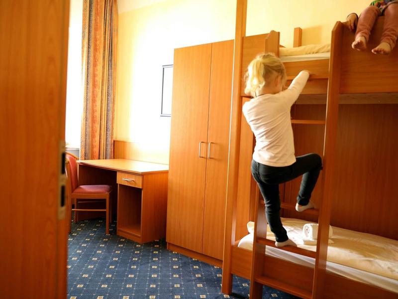 Kind klettert die Holzleiter zum oberen Stockbett in einem hellen Zimmer mit Schreibtisch und Schrank.