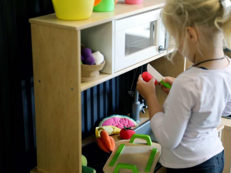 Kind spielt mit Spielzeug in einer Küche aus Holz mit bunten Kunststoffteilen.