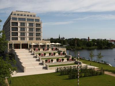 Modernes Gebäude mit Terrassen und Treppen, umgeben von Grünfläche und Fluss im Hintergrund.