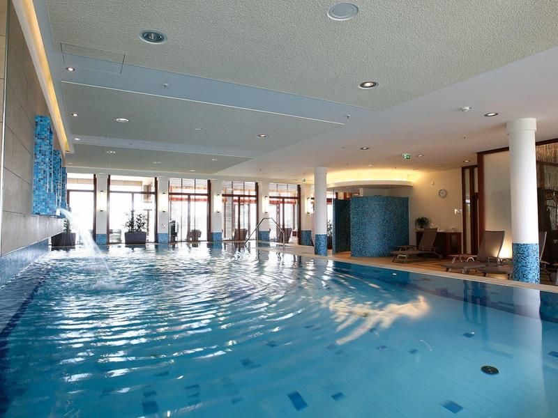 Moderner Innenpool mit blauen Fliesen, großem Fensterfront und loungigem Sitzbereich am Rand.