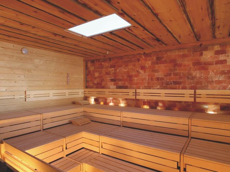 Großer Holzsauna-Raum mit L-förmigen Sitzbänken und Ziegelwand, warmes Licht von unten.