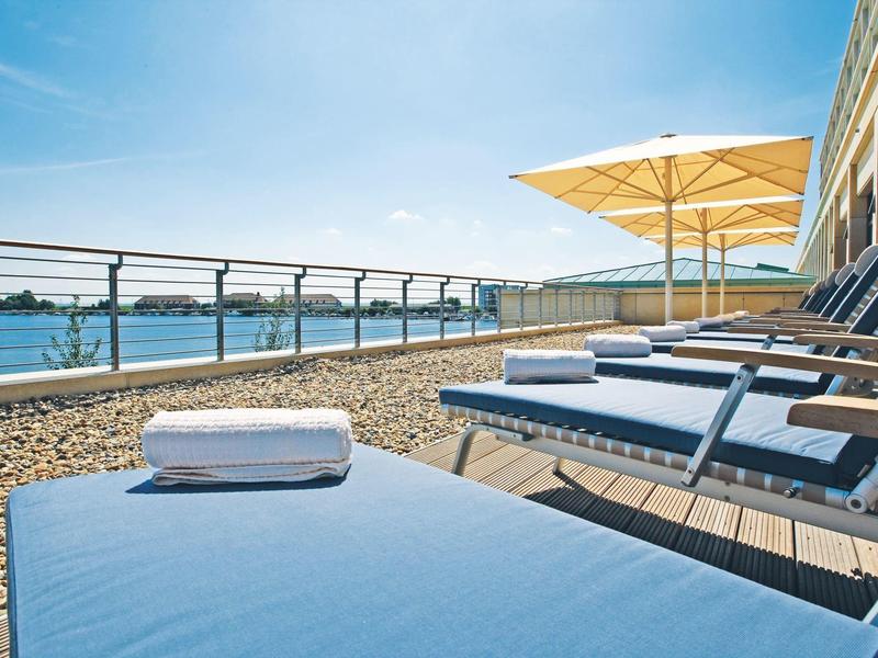 Mehrere blaue Liegestühle mit Handtüchern stehen auf einer Terrasse mit Sonnenschirmen.