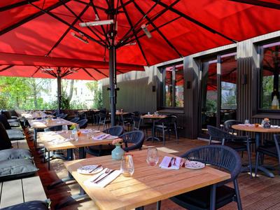 Gemütliche Außenterrasse eines Restaurants mit Holztischen und roten Sonnenschirmen.