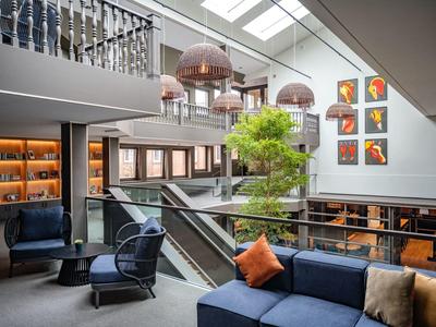 Lounge d'hotel moderno con divani blu, cuscini arancioni, un albero e arte contemporanea alle pareti.