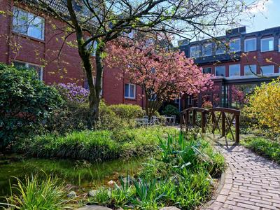 Garten mit blühendem Baum und gepflastertem Weg neben einem mehrstöckigen Hotelgebäude.