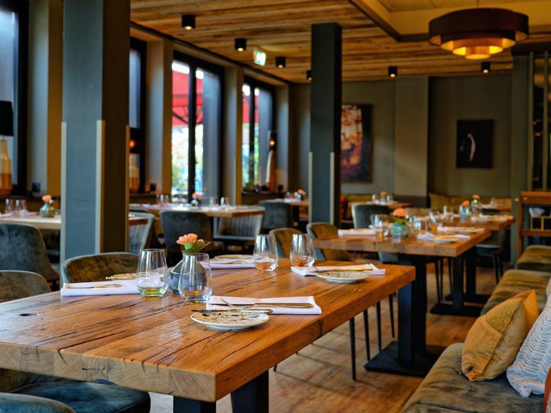 Ristorante accogliente con tavoli in legno, sedie, ampie finestre e illuminazione calda.