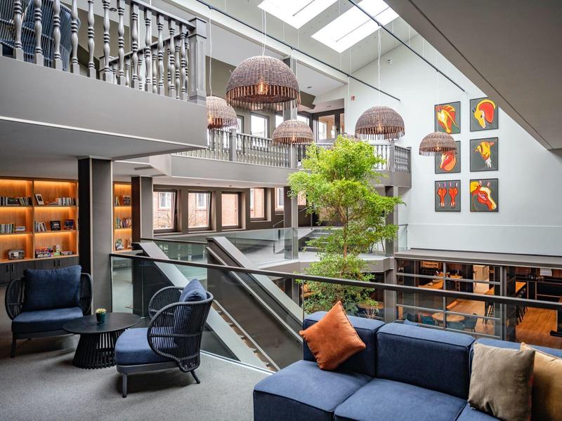 Lounge d'hotel moderno con divani blu, cuscini arancioni, un albero e arte contemporanea alle pareti.