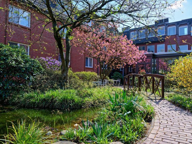 Un giardino con alberi in fiore, cespugli e un piccolo ponte vicino a un edificio dell'hotel