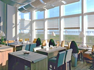 Helles Restaurant mit großen Fenstern und modernem Mobiliar bei Tageslicht.