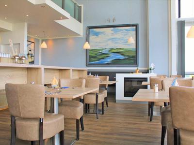 Helles Restaurant mit beigen Stühlen, Holzboden und großem Landschaftsgemälde an der Wand.