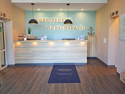 Heller Hotel-Empfangsbereich mit Tresen, digitalem Check-in Terminal und Prospektständern.