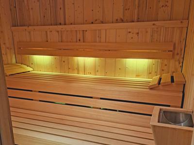 Gemütliche Holzbänke in einer Sauna mit indirekter Beleuchtung und einem Wassereimer.