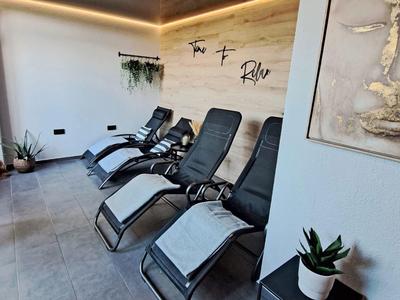 Modernes Ruheraum mit schwarzen Liegestühlen, Handtüchern und Pflanzen an den Wänden.