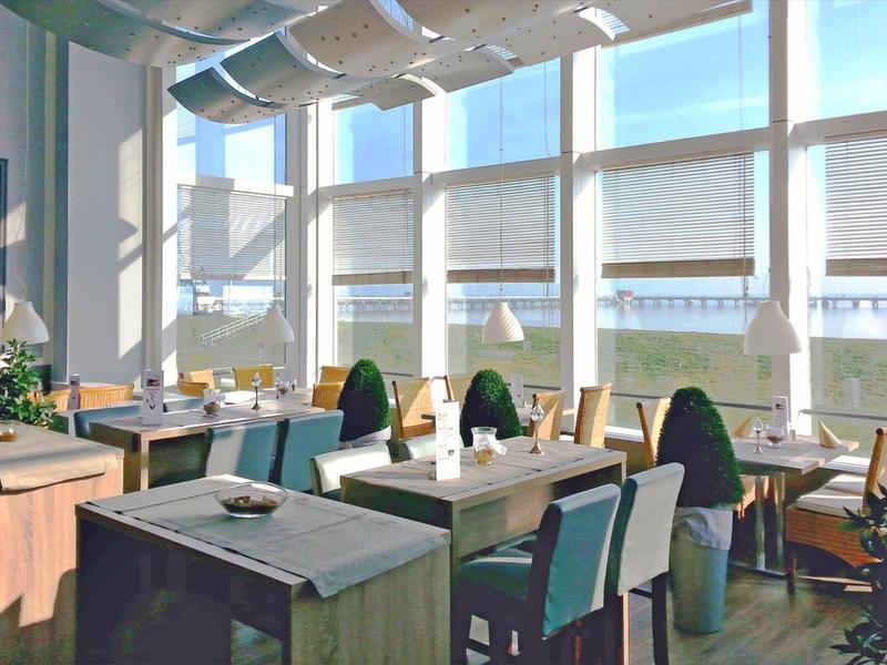 Hell beleuchteter Hotel-Restaurantbereich mit modernen Tischen und Stühlen neben großen Fenstern.