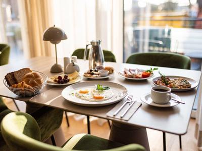 Une table de petit déjeuner dressée avec café, croissants et divers plats dans un restaurant lumineux.
