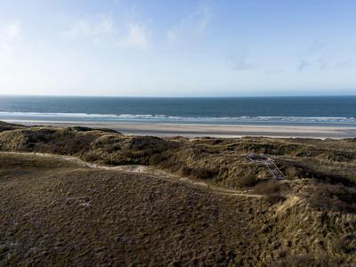 Vaste paysage de dunes avec plage et mer calme sous un ciel légèrement nuageux