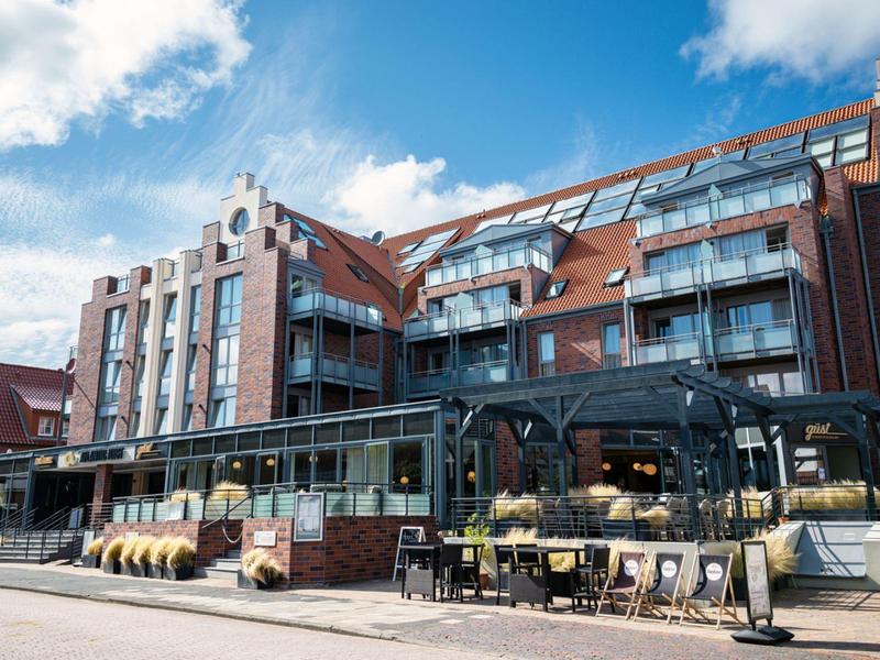Bâtiment moderne en briques rouges avec balcons en verre et restaurant au rez-de-chaussée par temps ensoleillé.