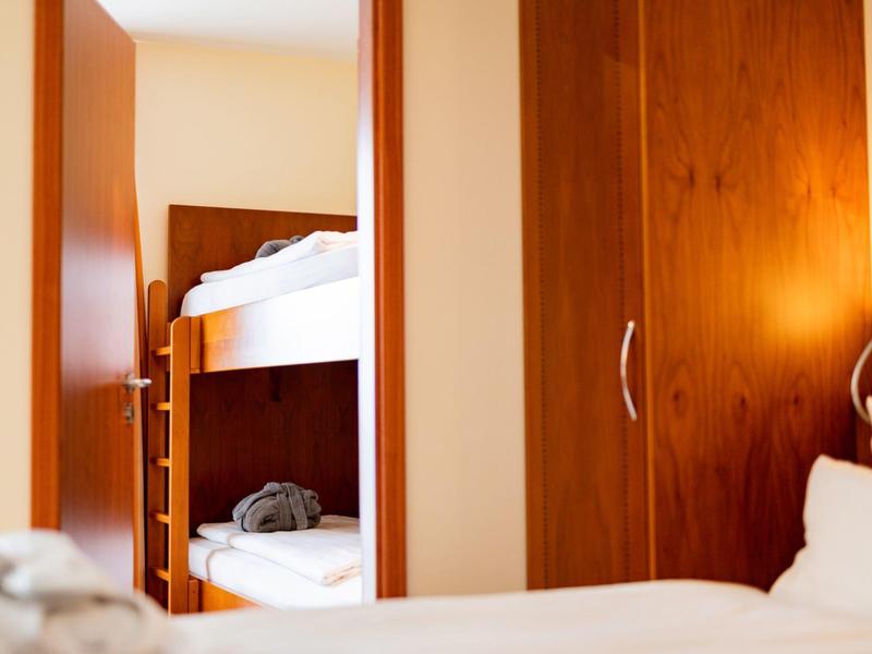 Vue d'une chambre d'hôtel avec lits superposés et meubles en bois sous une lumière chaude.