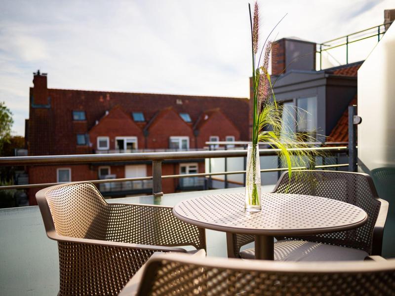 Table de balcon avec plateau en verre, deux chaises et un vase avec plante devant des bâtiments