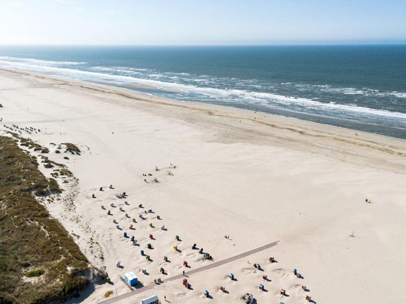 Grande plage avec dunes de sable, chaises longues éparpillées et vue sur la mer calme.