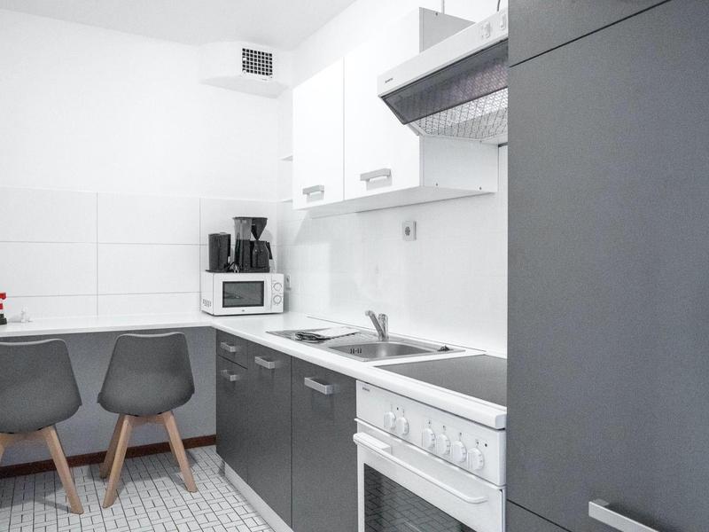 Moderne kleine Küche mit weißen und grauen Schränken, Herd, Mikrowelle und zwei grauen Stühlen.