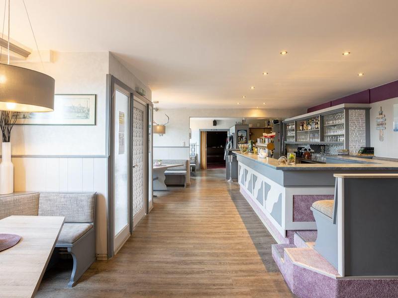 Helles Restaurant mit Holzboden, Theke rechts, grauen Sitzbänken und Deckenlampen.