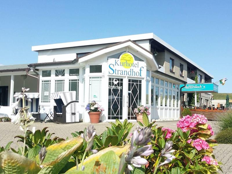 Modernes helles Café mit großer Terrasse und bunten Blumen im Vordergrund.