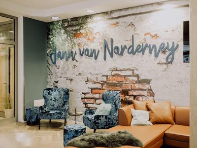 Modernes Wohnzimmer mit blauen Sesseln, brauem Ledersofa und Wandkunst mit "Paris van Norderney".