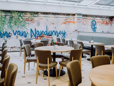 Restaurant mit Holztischen und gepolsterten Stühlen vor einer Wand mit Graffiti und Fenstern