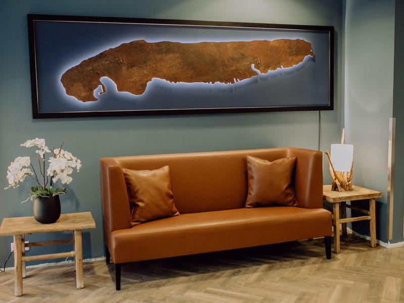 Moderní obývací pokoj s hnědou koženou pohovkou, dvěma stolky a nástěnným uměním.