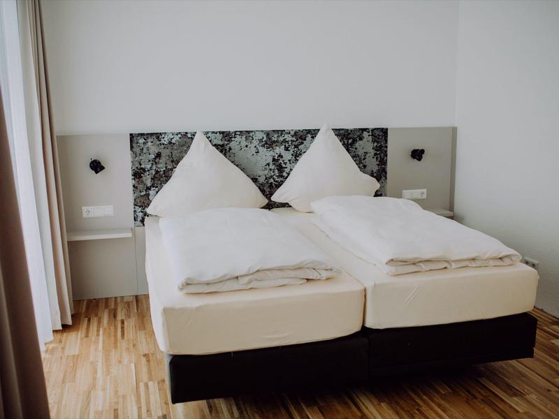 Moderní hotelový pokoj se dvěma jednolůžky, bílým povlečením a vzorovaným čelem postele.