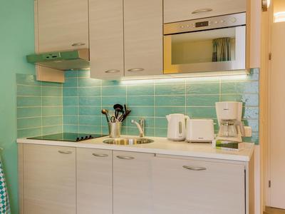 Kleine keuken met blauwe tegels, witte kastjes en moderne apparaten in een hotelkamer.