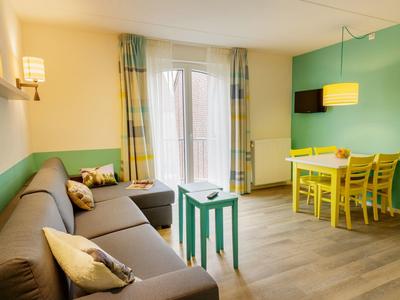 Lichte woon- en eetkamer met bank, klein tafeltje, eettafel met stoelen en aan de muur gemonteerde tv.