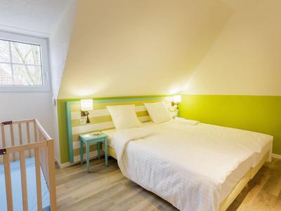 Licht ingericht slaapkamer met groene accenten, tweepersoonsbed en raam onder hellend dak.